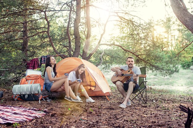 Fiesta, campamento de grupo de hombres y mujeres en el bosque. relajante, cantando una canción contra la hierba verde.