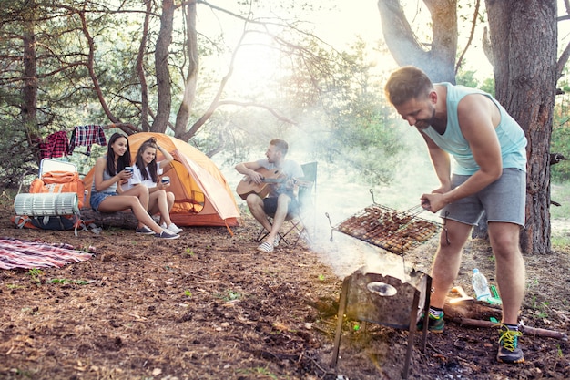 Fiesta, campamento de hombres y mujeres en el bosque. Se relajan, cantan una canción y cocinan barbacoa