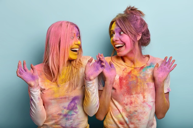 Fiesta y concepto de vacaciones de colores. Las mujeres europeas optimistas levantan la mano y discuten algo alegremente, se divierten juntas, juegan con los colores, expresan buenas emociones. Festival de Holi en India