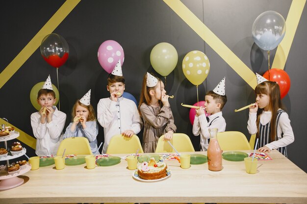 Fiesta de cumpleaños divertida para niños en habitación decorada. Niños felices con pastel y globos.