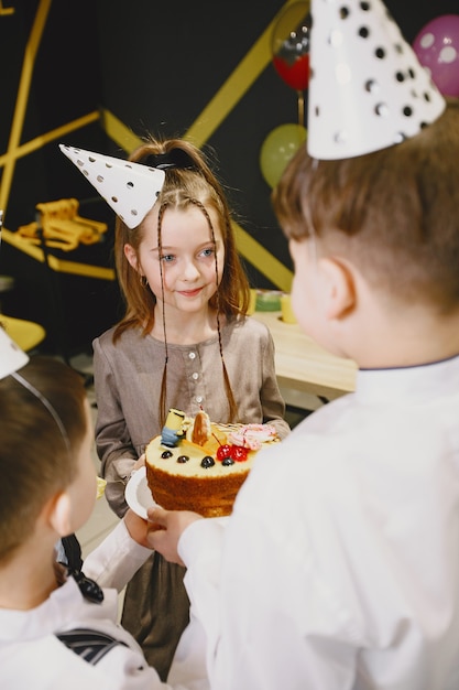 Fiesta de cumpleaños divertida para niños en habitación decorada. Niños felices con pastel y globos.