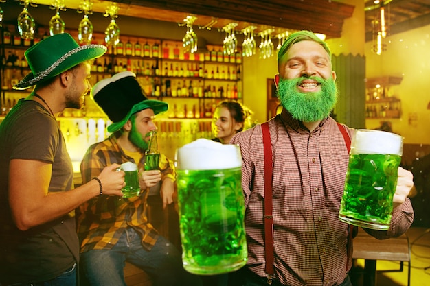Fiesta del día de San Patricio. Amigos felices está celebrando y bebiendo cerveza verde. Hombres y mujeres jóvenes con sombreros verdes. Interior del pub.