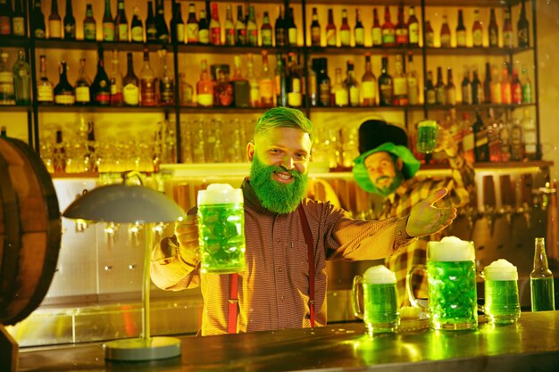 Fiesta del día de San Patricio. Amigos felices está celebrando y bebiendo cerveza verde. Hombres y mujeres jóvenes con sombreros verdes. Interior del pub.