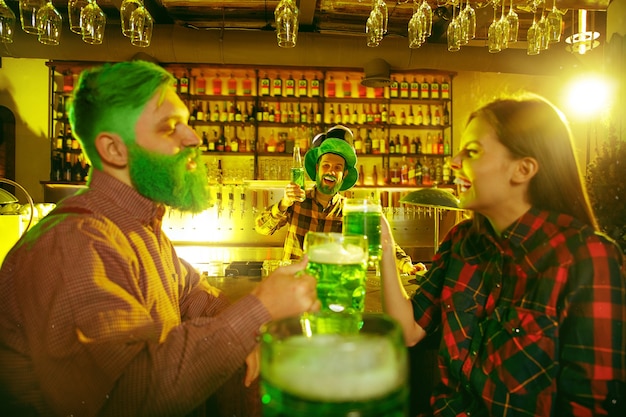 Fiesta del día de San Patricio. Amigos felices están celebrando y bebiendo cerveza verde. Hombres y mujeres jóvenes con sombreros verdes. Interior del pub.