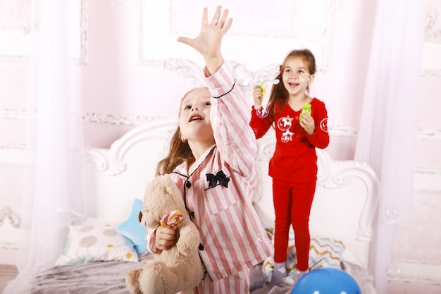 Fiesta de pijamas para niños, divertidas hermanas felices vestidas con pijamas brillantes, juego de burbujas