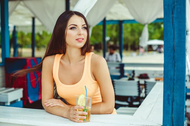 Fiesta de verano de estilo de vida. Mujer joven sexy con el pelo largo bebiendo cócteles en el bar de la playa.
