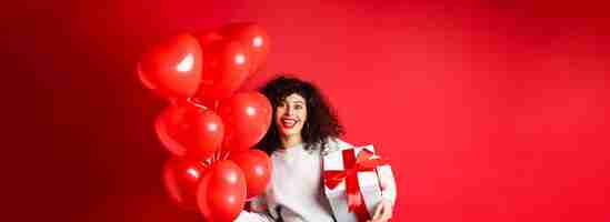 Foto gratuita fiestas y celebración feliz cumpleaños niña sosteniendo regalo y posando cerca de fiesta globos de helio smil