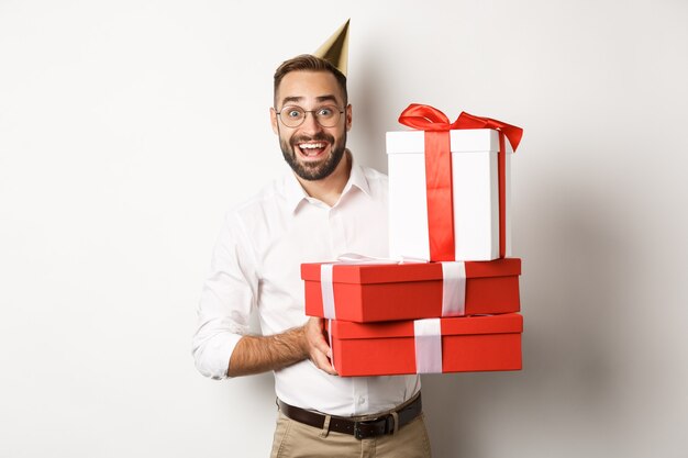 Fiestas y celebraciones. Hombre feliz recibiendo regalos en cumpleaños, sosteniendo regalos y mirando emocionado, de pie