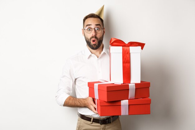 Fiestas y celebraciones. Hombre feliz recibiendo regalos en cumpleaños, sosteniendo regalos y mirando emocionado, de pie