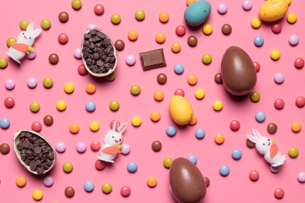 Foto gratuita figuras de conejo; huevos de pascua; gemas multicolores sobre fondo rosa