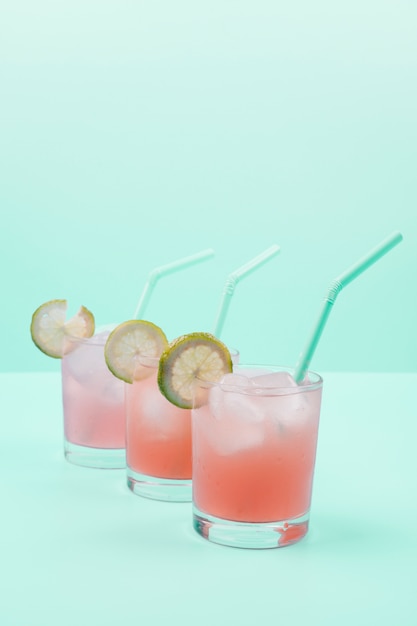 Fila de copas de cóctel con cubitos de hielo; pajita; Rodajas de limón sobre fondo de menta
