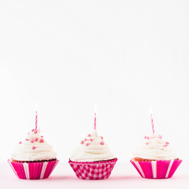 Foto gratuita fila de cupcakes frescos con velas encendidas sobre fondo blanco