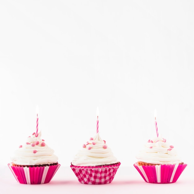 Fila de cupcakes frescos con velas encendidas sobre fondo blanco