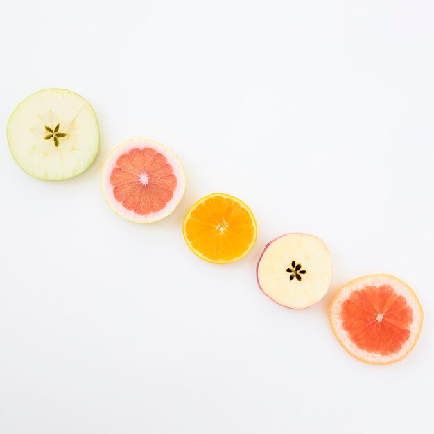 Fila diagonal de rodajas de manzana; Rodajas de pomelo y naranja sobre fondo blanco