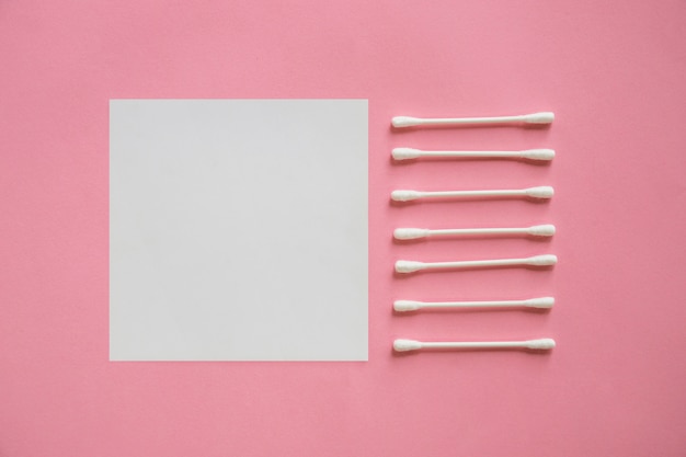 Foto gratuita fila de hisopos de algodón cerca de la nota adhesiva en blanco sobre fondo rosa
