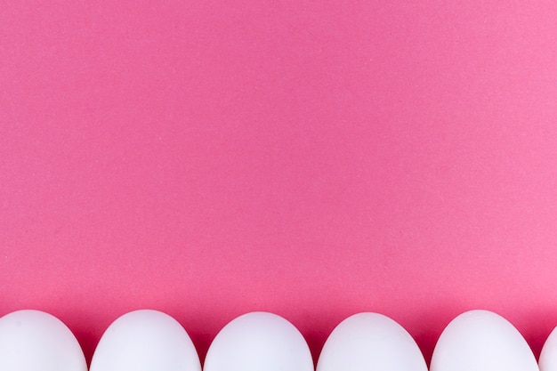 Fila de huevos blancos en mesa rosa