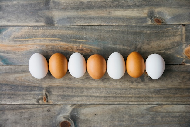 Foto gratuita fila de huevos de color marrón y blanco en tablón de madera