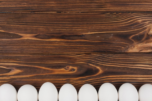 Fila de huevos de gallina blanca en mesa de madera marrón