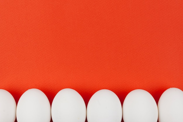 Fila de huevos de gallina blanca en mesa roja