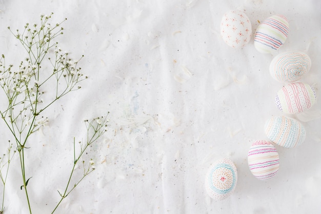 Fila de huevos de Pascua con patrones cerca de ramita de planta y plumas en textil