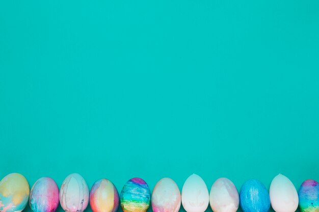 Fila de huevos de Pascua pintados en la parte inferior de fondo turquesa