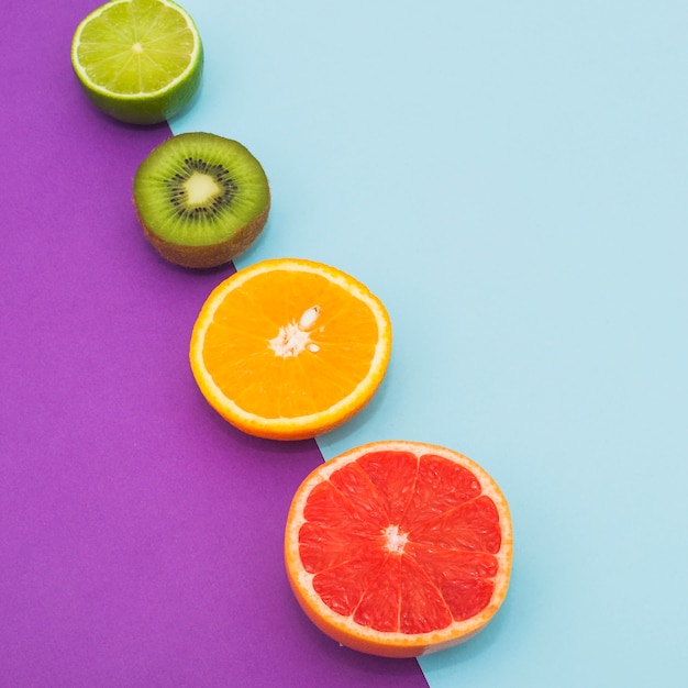 Fila inclinada de frutas cítricas y kiwi sobre fondo azul y púrpura doble