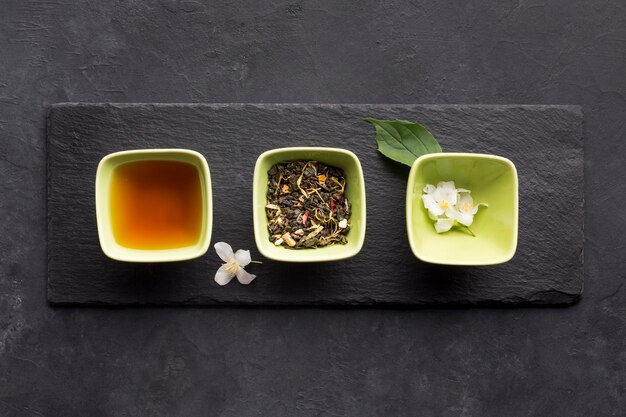 Fila de ingrediente de té saludable y flor de jazmín blanco en piedra de pizarra