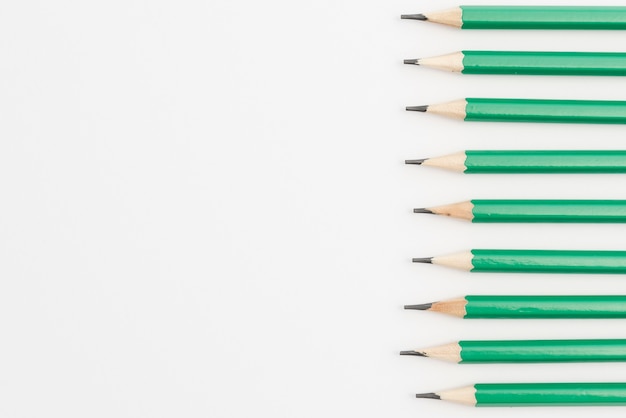 Fila de lápices afilados verdes sobre fondo blanco.