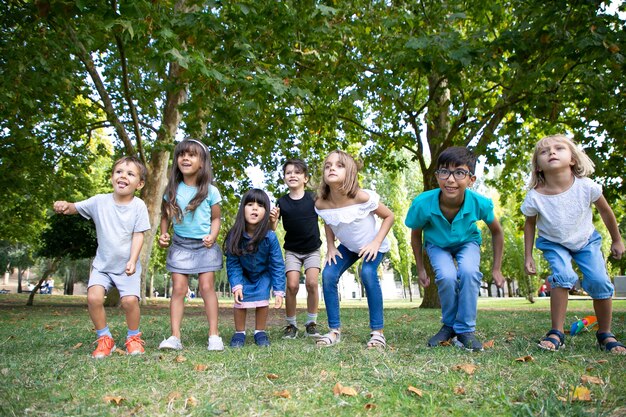 Fila de niños alegres haciendo sentadillas juntos en el parque, mirando a otro lado con emoción. Concepto de fiesta o entretenimiento para niños