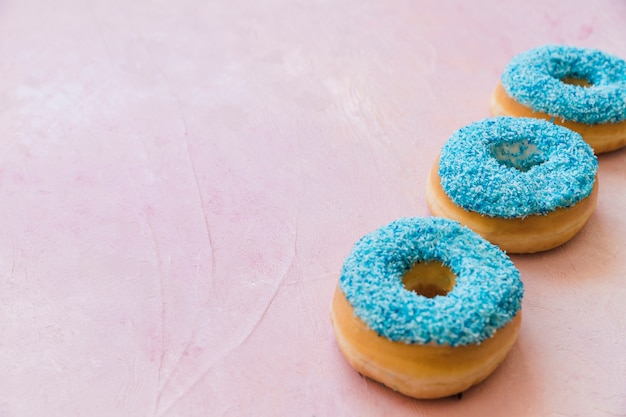 Fila de tres rosquillas azules en una fila en fondo rosado