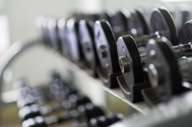 Filas de pesas de metal en rack en el gimnasio / club deportivo. Equipo del entrenamiento del peso.