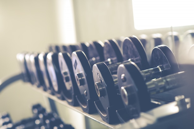 Filas de pesas de metal en rack en el gimnasio / club deportivo. Equipo del entrenamiento del peso.