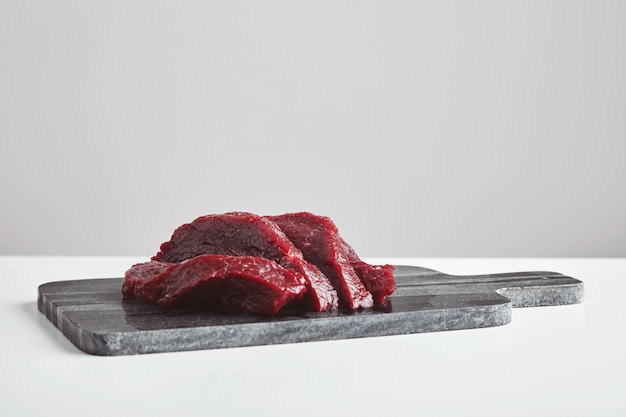 Filete de carne de ballena cruda de primera calidad en rodajas sobre una tabla de cortar de piedra de mármol aislada en el cuadro blanco.