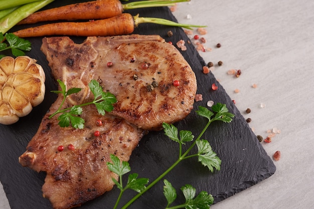 Filete de cerdo a la parrilla de una barbacoa de verano servido con verduras, espárragos, zanahorias baby, tomates frescos y especias. bistec a la plancha sobre pizarra negra sobre superficie de piedra. vista superior.