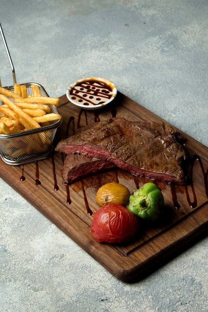 Filete cocido raro servido con papas fritas, verduras a la parrilla y salsa