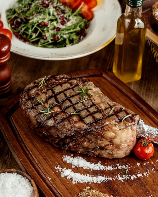 Filete a la parrilla con hierbas saladas y tomate a la parrilla servido sobre tabla de madera