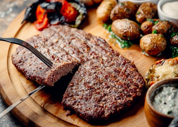 Filete con patatas fritas y verduras sobre tabla de madera