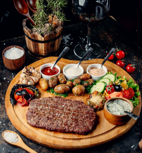 Filete con patatas y verduras sobre tabla de madera