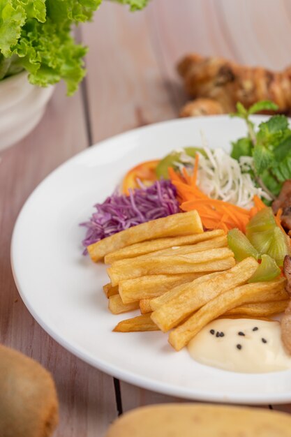 Filete de pescado con papas fritas, kiwi, lechuga, zanahorias, tomates y repollo en un plato blanco.