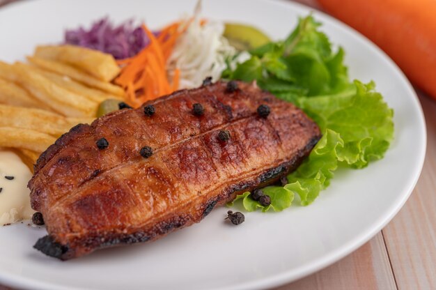 Filete de pescado con papas fritas, kiwi, lechuga, zanahorias, tomates y repollo en un plato blanco.