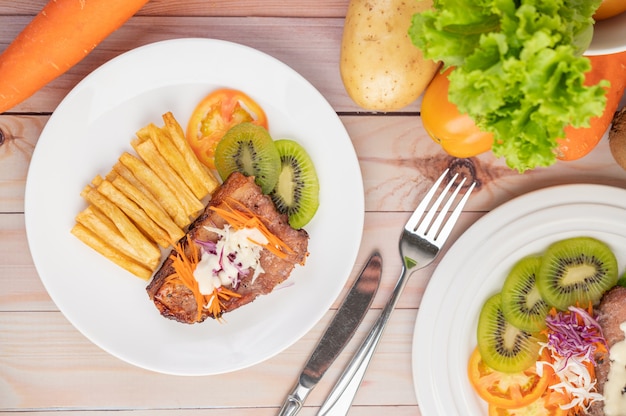 Filete de pescado con papas fritas, kiwi, lechuga, zanahorias, tomates y repollo en un plato blanco.