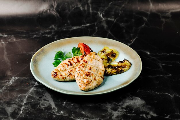 Filete de pescado a la parrilla con berenjenas y servido con tomate y perejil.