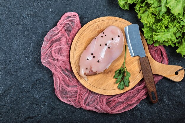 Filete de pollo crudo sobre tabla de madera con verduras y cuchillo.