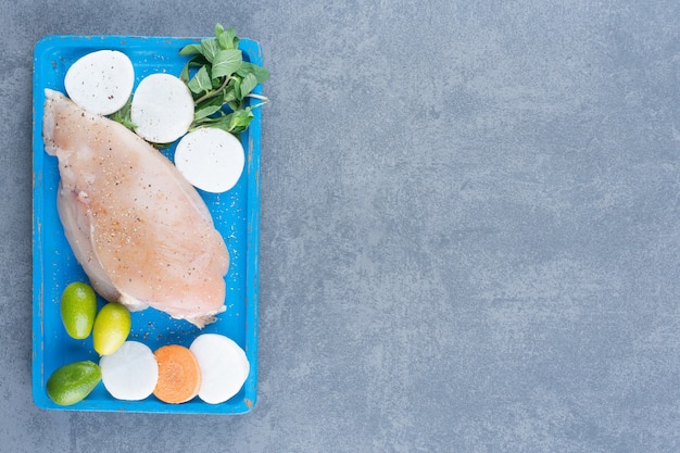 Foto gratuita filete de pollo crudo con verduras frescas en tablero azul.