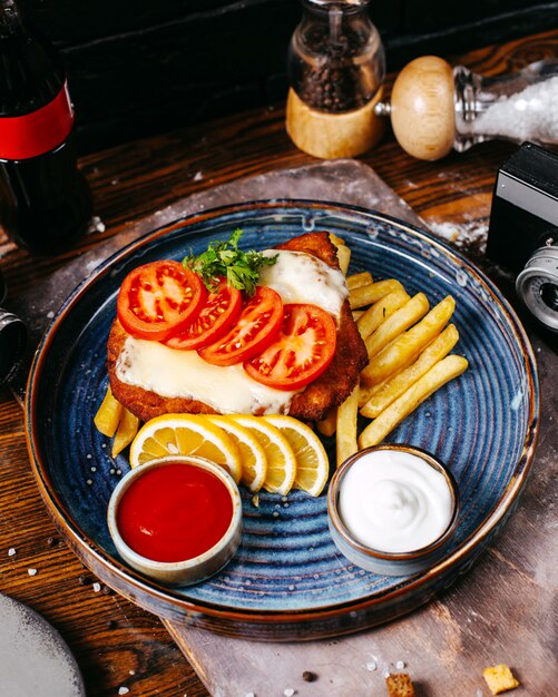 filete de pollo empanado frito con queso servido con rodajas de tomates, limones y papas fritas