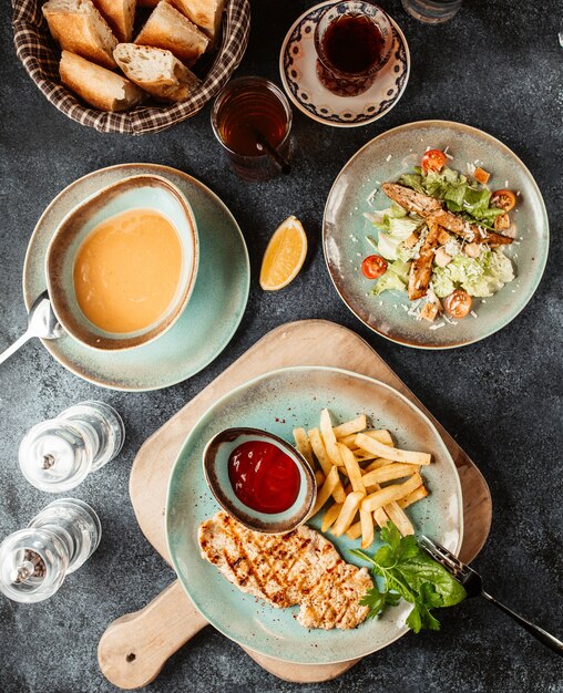 Filete de pollo con papas fritas y salsa de tomate servido con sopa y ensalada César