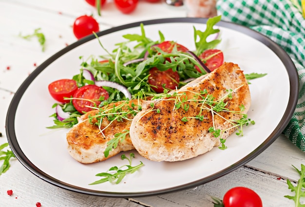 Filete de pollo a la parrilla y ensalada de vegetales frescos de tomate, cebolla roja y rúcula. Ensalada de carne de pollo. Comida sana.