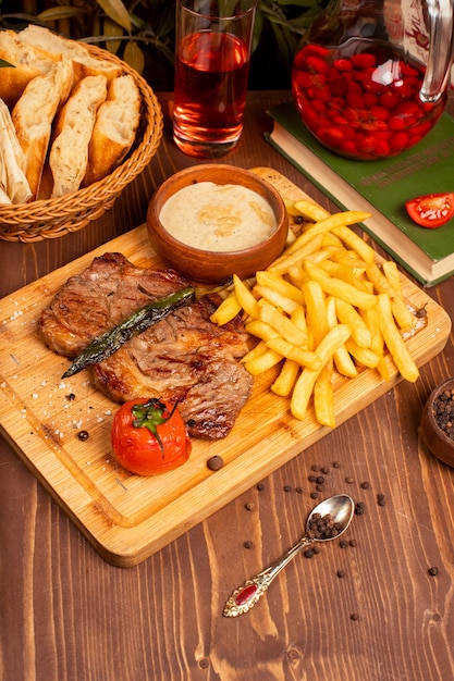 Foto gratuita filete de ternera con papas fritas, salsa de mayonesa con crema agria y hierbas en un plato de madera