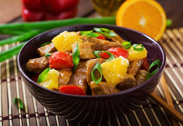 Filete de ternera - salteado con naranjas y pimentón en salsa agridulce sobre una mesa de madera.