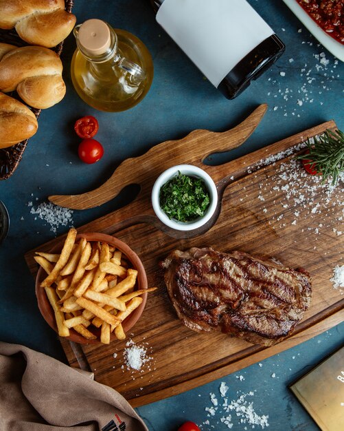 Filete de ternera servido con papas fritas y hierbas gren en cubitos sobre tabla de madera